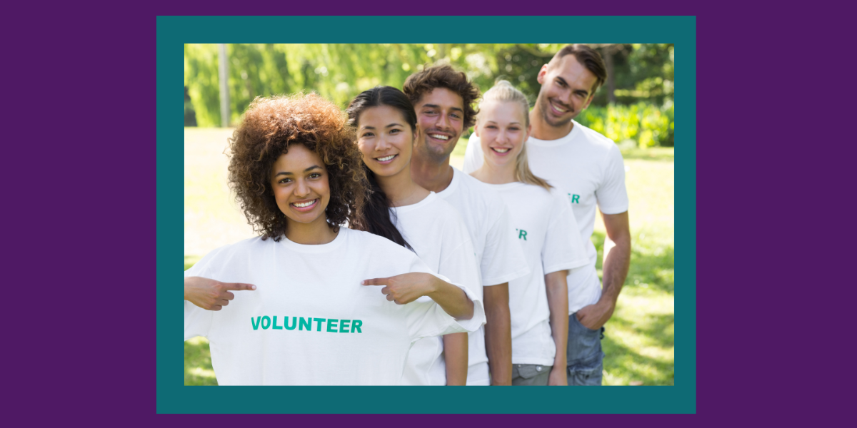 Five diverse individuals all wearing a white shirt with the word “Volunteer” on it lined up in a row while standing outside.